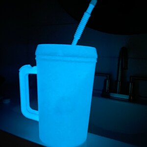 Op de afbeelding: Een witte plastic beker met een blauwe gloed en een witte rietje. De beker heeft een handvat en staat op een wit oppervlak.