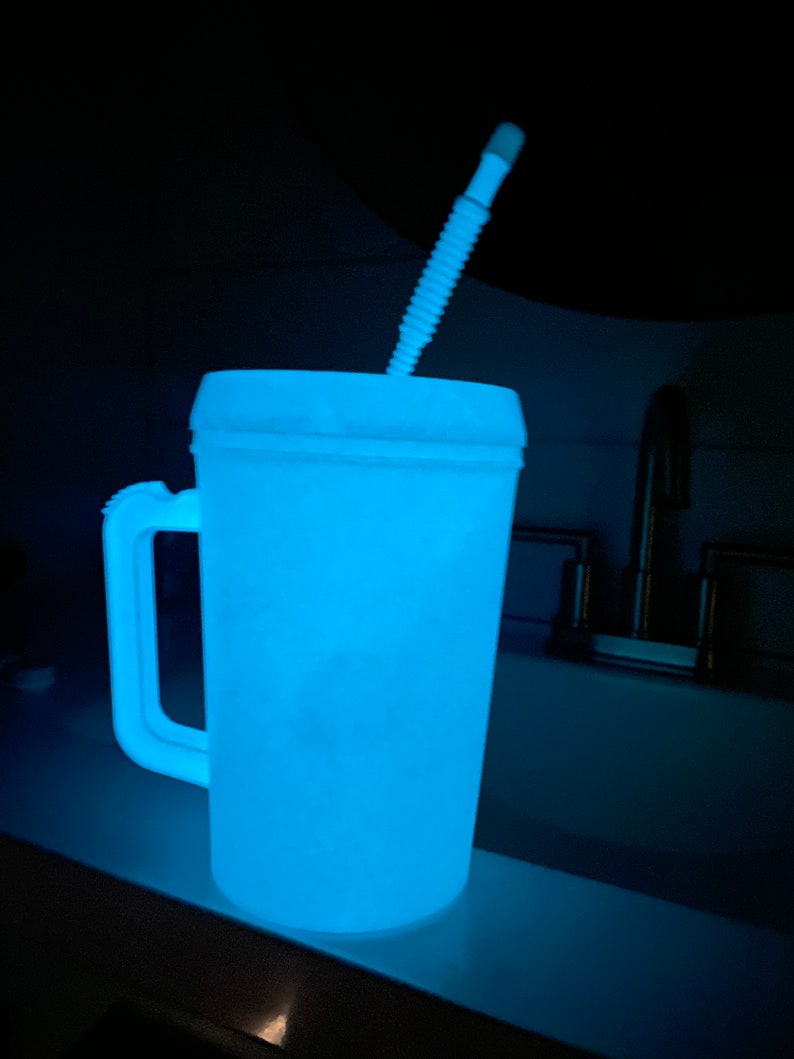 Op de afbeelding: Een witte plastic beker met een blauwe gloed en een witte rietje. De beker heeft een handvat en staat op een wit oppervlak.