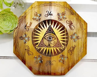 May include: Wooden octagonal board with a sunburst design and an all-seeing eye in the center. The board has the words "Yes", "No", "True", "False", "Now", "Wait", and "Maybe" inscribed around the edge.