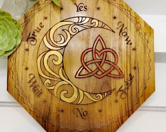 May include: Wooden octagonal board with a Celtic knot design in red and gold, surrounded by a crescent moon with a gold and white design. The board has the words "Yes", "No", "True", "False", "Wait", and "Now" inscribed around the edge.