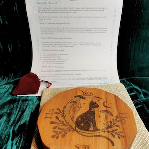 Op de afbeelding: Een houten pendelbord met een zwart kattenontwerp en de woorden "Ja" en "Nee" erop. Het bord is omringd door een halve maan en paddenstoelen. De tekst "Moore Designs Australia" staat onderaan het bord.