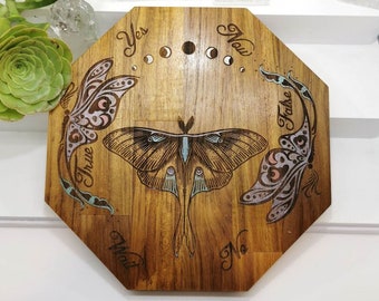 May include: Wooden octagonal board with a moon phase design and a moth illustration. The board has the words "Yes", "Now", "False", "True", "Wait", and "No" inscribed around the edge.