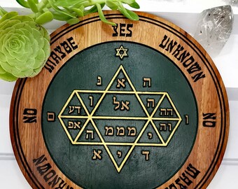 Könnte beinhalten: Ein rundes Holz-Divinationsbrett mit grünem Zentrum und goldenen hebräischen Buchstaben. Das Brett hat die Wörter "JA", "VIELLEICHT", "UNBEKANNT" und "NEIN" am Rand.
