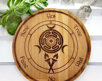 May include: Wooden Ouija board with a circular design featuring a labyrinth, three crescent moons, and two torches. The board has the words "Yes", "No", "True", "False", "Wait", and "Now" inscribed around the edge.