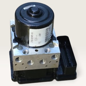 Peut inclure: Une unité de commande hydraulique ABS automobile noire et argentée comprenant un moteur cylindrique sur le dessus, un bloc métallique avec plusieurs ports filetés et un boîtier de connecteur électrique en plastique noir sur le côté.