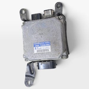 Puede incluir: Una unidad de control electrónico de metal plateado para vehículo, con una etiqueta azul y blanca con el texto TOYOTA 89650-53010, JTEKT, R 1 EPS 12V y un código de barras. La unidad tiene conectores de plástico negro y soportes de montaje.