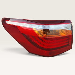 Puede incluir: Un conjunto de luz trasera para vehículo con una forma curva y aerodinámica, que presenta una lente roja prominente, una sección horizontal blanca transparente en la parte superior y un indicador de giro ámbar integrado en el lateral.