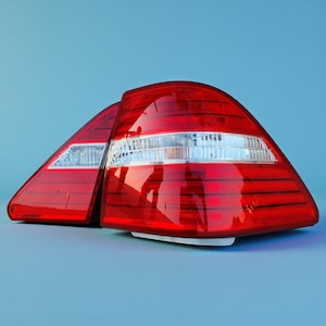 May include: A pair of automotive tail light assemblies featuring a curved, triangular shape with a glossy red lens and a horizontal clear white section. The lights have a ribbed texture across the red surface and a smooth finish on the clear area.