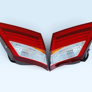 Puede incluir: Un par de luces traseras para vehículos con un diseño angular y afilado. Cada unidad tiene una sección de lente roja grande con crestas horizontales, una sección inferior transparente para reversa y un segmento ámbar.