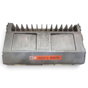 May include: A gray metal JBL audio amplifier featuring a heat sink with vertical fins on the top edge. An orange label on the front displays the text JBL, 86280-0C130, HARMAN/BECKER USA, and SEQUOIA, along with a small square QR code graphic.