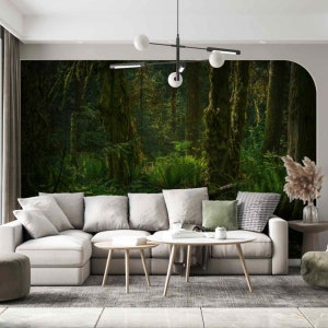 May include: A white sectional sofa with a light grey rug in front of it. The sofa has several cushions, including a green one and a black and white patterned one. There is a coffee table in front of the sofa and a side table to the left of the sofa. The wall behind the sofa has a large mural of a lush green forest with tall trees and moss.