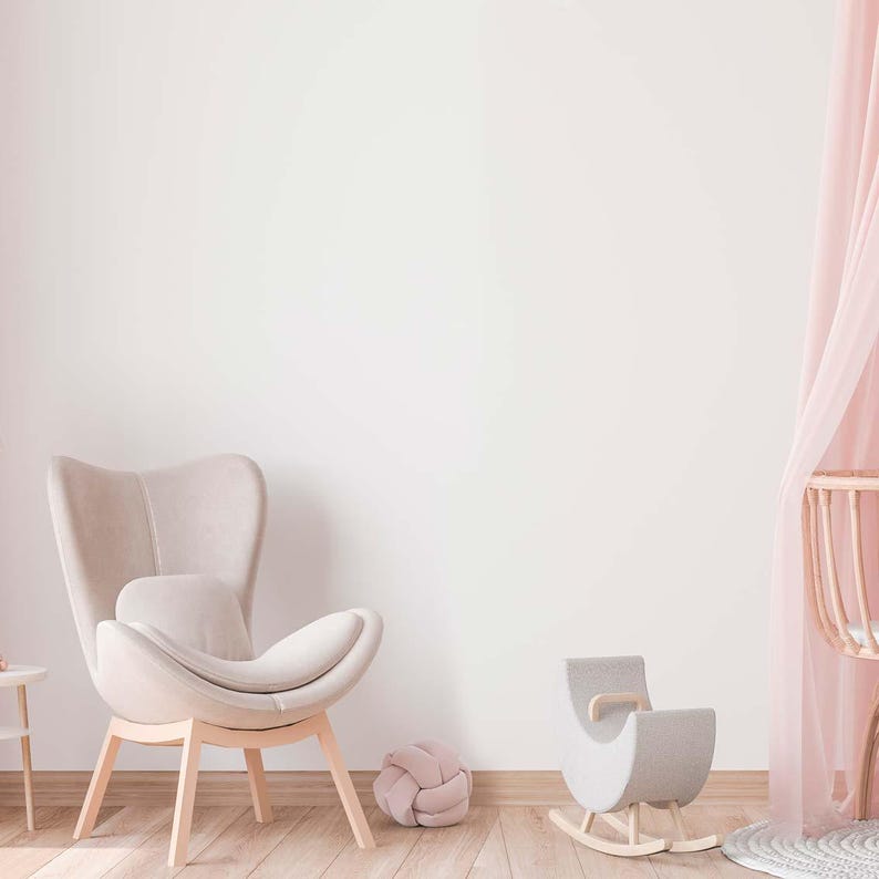 May include: A light pink canopy hangs over a wooden crib in a nursery. A light gray rocking horse sits in front of the crib. A light gray armchair with a light gray pillow sits in the foreground. A light gray knotted ball sits on the floor.