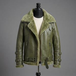May include: An olive green leather jacket featuring a thick, matching olive shearling lining and oversized collar. The jacket includes a front zipper closure, two zippered side pockets, and adjustable buckled straps on the cuffs and waist.