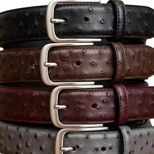 Puede incluir: Una pila de cinturones de cuero en varios colores: negro, marr&oacute;n, burdeos y gris. Cada cintur&oacute;n presenta una hebilla plateada y una superficie texturizada con peque&ntilde;as hendiduras espaciadas uniformemente. Un accesorio cl&aacute;sico.