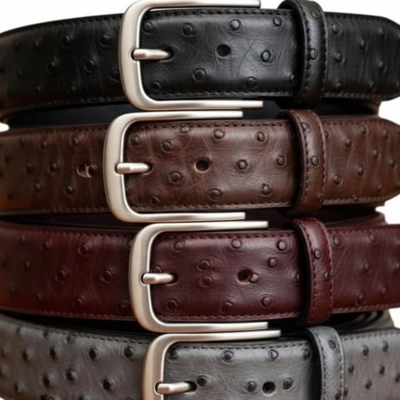 Puede incluir: Una pila de cinturones de cuero en varios colores: negro, marr&oacute;n, burdeos y gris. Cada cintur&oacute;n presenta una hebilla plateada y una superficie texturizada con peque&ntilde;as hendiduras espaciadas uniformemente. Un accesorio cl&aacute;sico.