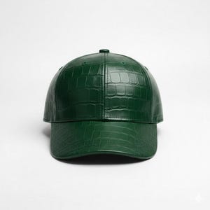 May include: A dark green baseball cap with a textured, crocodile-like pattern. The cap has a curved brim and a small button on top. The hat is made of a shiny material and is set against a white background.