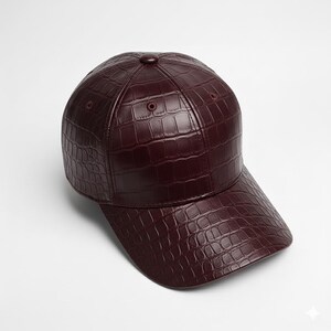 May include: A burgundy baseball cap with a textured, crocodile-like pattern. The cap features a curved brim and a button on top. The hat is made of a leather-like material and is designed to be worn on the head.