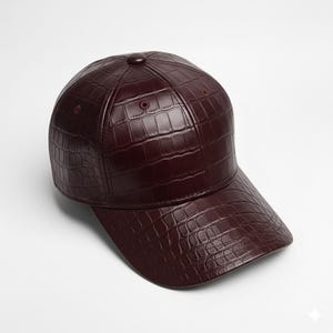 May include: A burgundy baseball cap with a textured, crocodile-like pattern. The cap features a curved brim and a button on top. The hat is made of a shiny material.