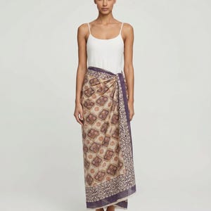 Full length hand block printed organic cotton sarong in a blue floral Indian pattern, tied as a side-knot beach wrap on a woman at the beach, showing the lightweight and breathable fabric.