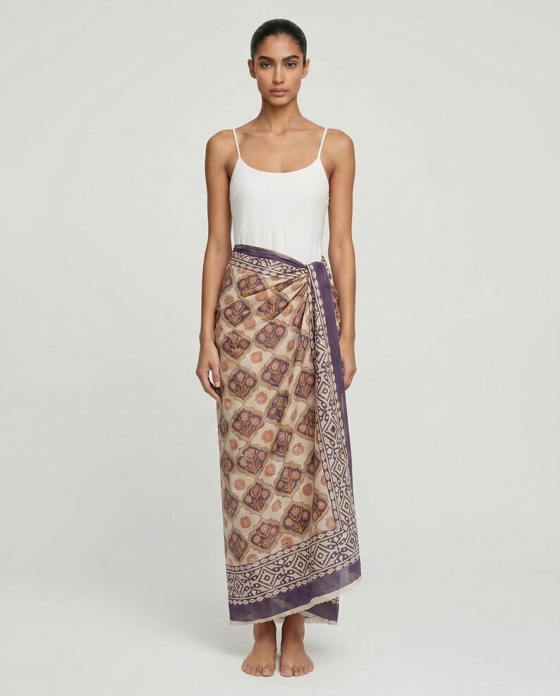 Full length hand block printed organic cotton sarong in a blue floral Indian pattern, tied as a side-knot beach wrap on a woman at the beach, showing the lightweight and breathable fabric.
