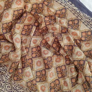 A lightweight cotton block print scarf draped over shoulders as a summer shawl, styled with a white linen dress to demonstrate the multi-way use of the large beach wrap.