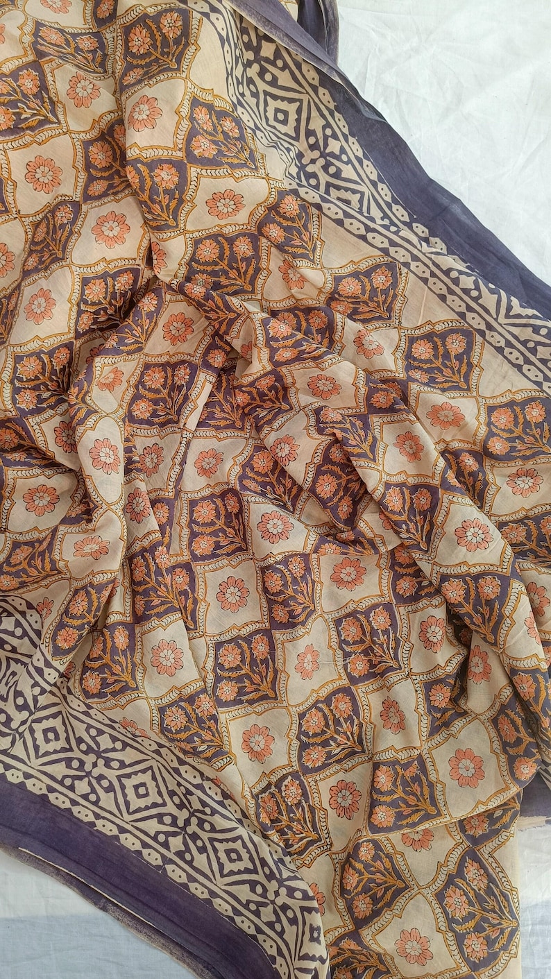 A lightweight cotton block print scarf draped over shoulders as a summer shawl, styled with a white linen dress to demonstrate the multi-way use of the large beach wrap.