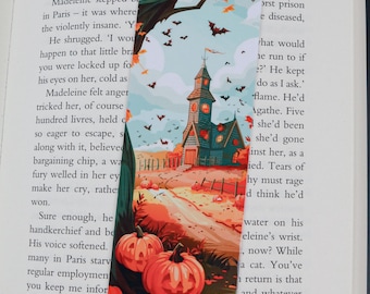 Puede incluir: Un marcapáginas decorativo con temática de Halloween. La ilustración muestra una casa embrujada, calabazas, murciélagos y hojas de otoño en tonos naranja, turquesa y marrón. El marcapáginas es rectangular.
