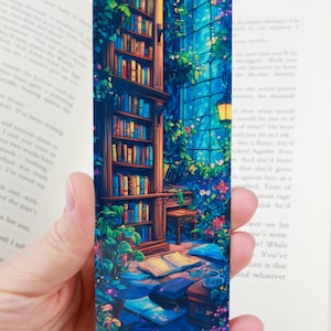 Può includere: Un segnalibro blu e verde con una libreria, una finestra e un tavolo con libri e una tazza di tè. Il segnalibro è illustrato in uno stile fantasioso e magico.