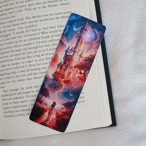 Könnte beinhalten: Ein farbenfrohes Lesezeichen mit einem Fantasie-Schloss, zu dem ein roter Weg führt. Das Schloss ist von einem sternenklaren Himmel mit einer Sichelmond umgeben. Eine Frau in einem blauen Kleid geht den Weg zum Schloss hinauf.