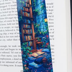 Può includere: Un segnalibro blu e verde con un dipinto di una libreria, una finestra e un tavolo con libri e una tazza. Il segnalibro ha uno sfondo blu scuro con una finestra blu chiaro e una pianta verde.