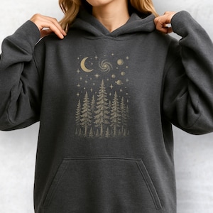 May include: Dark gray hoodie with a gold graphic of a crescent moon, stars, planets, and a forest of pine trees. The hoodie has a front pocket and a hood. The design is centered on the chest.