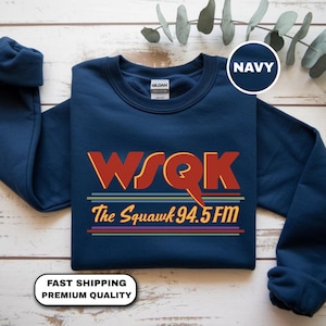 May include: Navy blue sweatshirt with the text "WSQK The Squawk 94.5 FM" in red and yellow, with colorful stripes. The sweatshirt has long sleeves and a crew neck.