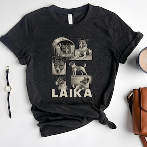May include: A dark gray t-shirt with a graphic of a dog in different poses. The text "LAIKA" is printed in white below the graphic.