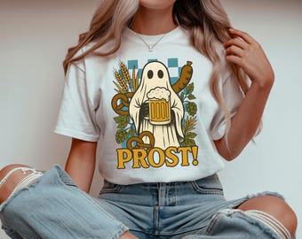 May include: White t-shirt featuring a cartoon ghost holding a beer stein and a sausage, with pretzels and wheat. The shirt has the word "PROST!" in a vintage style font. The design is in shades of beige, brown, and green.
