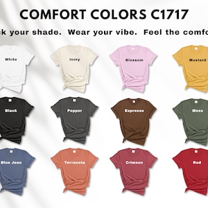 May include: A display of Comfort Colors C1717 t-shirts in various colors, including white, ivory, blossom, mustard, black, pepper, espresso, moss, blue jean, terracotta, crimson, and red. The text "Pick your shade. Wear your vibe. Feel the comfort." is at the top.