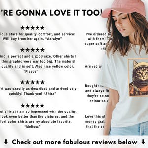 May include: White t-shirt featuring a cat astronaut graphic in a gold frame. The shirt has a crew neck and short sleeves. The image also includes customer reviews and the text "YOU'RE GONNA LOVE IT TOO!"