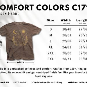 May include: Brown unisex t-shirt with a celestial cat graphic. The shirt features a crescent moon, sun, and wheat design. Sizes range from S (18 inches/46 cm width, 27 inches/69 cm length) to 3XL (28 inches/71 cm width, 33 inches/84 cm length).