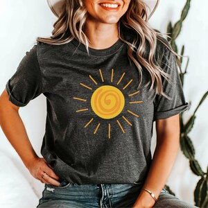 May include: Dark gray t-shirt featuring a yellow sun graphic with a spiral center and radiating lines. The shirt has short sleeves and a relaxed fit. The design is simple and cheerful, perfect for casual wear.