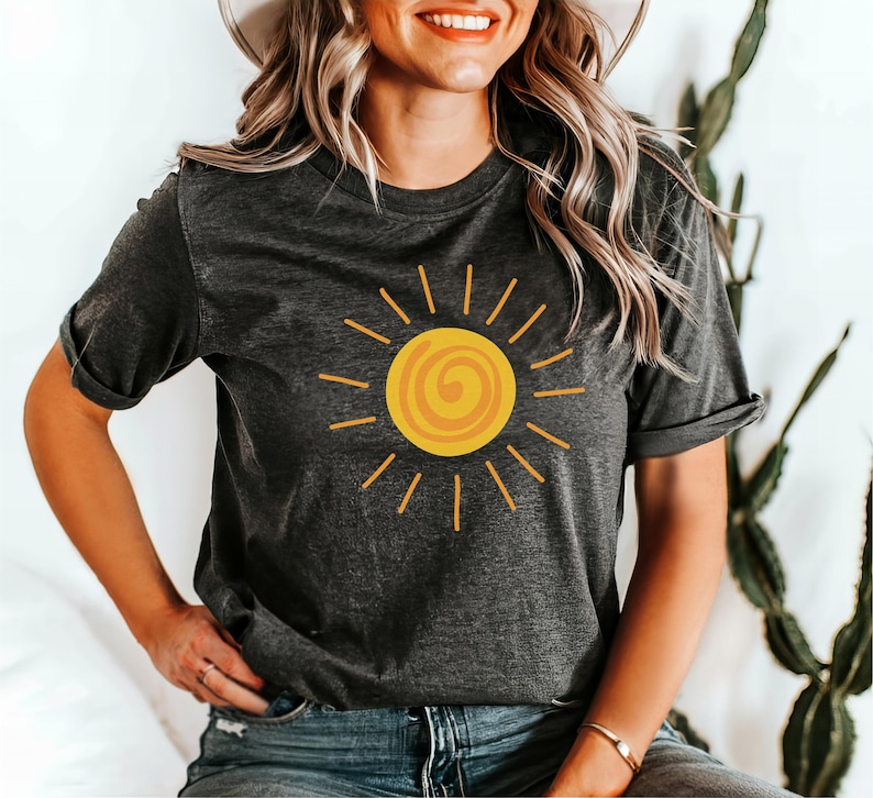 May include: Dark gray t-shirt featuring a yellow sun graphic with a spiral center and radiating lines. The shirt has short sleeves and a relaxed fit. The design is simple and cheerful, perfect for casual wear.