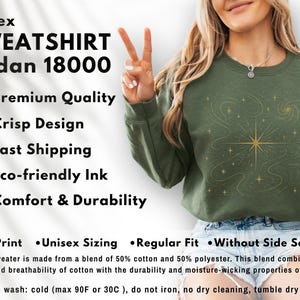 May include: Olive green unisex sweatshirt with a gold celestial design. The sweatshirt features the text "SWEATSHIRT Gildan 18000". The design includes a starburst and swirling lines. The sweatshirt is made of a blend of cotton and polyester.