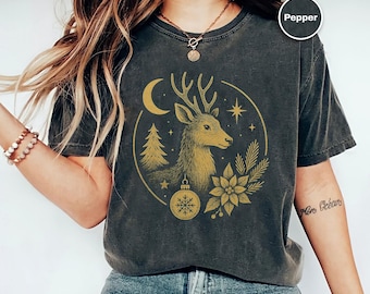 Puede incluir: Camiseta gris oscuro con una ilustración dorada de un ciervo, una luna creciente, un árbol de Navidad y un adorno de copo de nieve. La palabra "Pepper" está en un círculo blanco en la parte superior derecha.