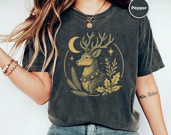 Puede incluir: Camiseta gris oscuro con una ilustración dorada de un ciervo, una luna creciente y estrellas. El ciervo está rodeado de hojas y bayas. La palabra "Pepper" está en un círculo en la parte superior derecha.