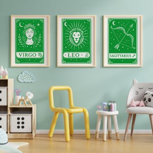 May include: Three green framed prints with white zodiac signs. The signs are Virgo, Leo, and Sagittarius. The prints are hanging on a light blue wall.