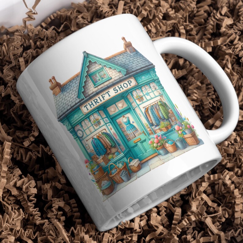 May include: White ceramic mug with a watercolour illustration of a teal Thrift Shop. The shop has a sign, clothing racks, and flower baskets. The mug has a white handle.