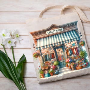 May include: A beige tote bag with a watercolour illustration of a thrift shop. The shop has a blue and white striped awning, brick facade, and a sign that reads "THRIFT SHOP". The shop is decorated with potted plants and hanging baskets.