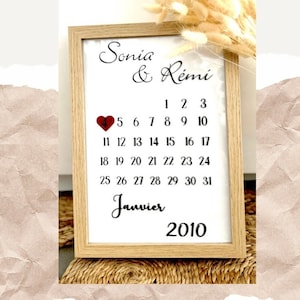 Peut inclure: Un calendrier encadré avec les noms Sonia & Rémi et un cœur rouge marquant le 4 janvier 2010. Le calendrier est entouré d'herbe de la pampa séchée.