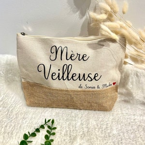 Op de afbeelding: Een beige canvas toilettas met een bruine jute bodem. De tas heeft zwarte tekst die "M&egrave;re Veilleuse de Sonia & Micka" luidt met een rood hart.