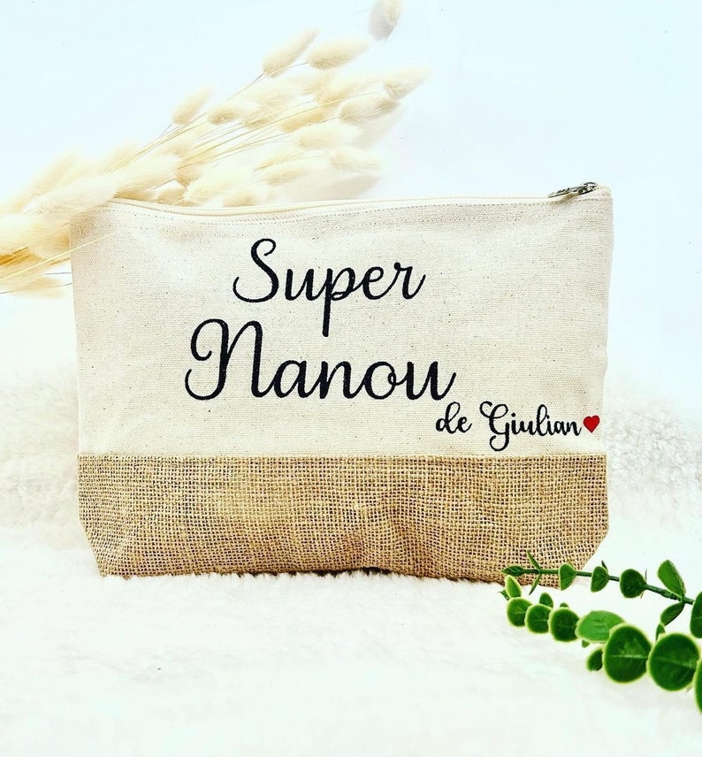 Op de afbeelding: Een beige canvas en jute toilettas met zwarte borduurwerk dat "Super Nanou de Giulian" met een rood hartje zegt.