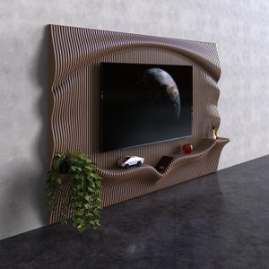 Puede incluir: Una unidad de entretenimiento de pared moderna, ondulada y de madera con una pantalla de televisión negra, un pequeño coche de juguete y un libro en un estante. La unidad tiene un acabado de madera natural y un diseño único y orgánico.