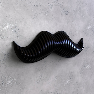 Puede incluir: Una decoración de pared de bigote negro tridimensional hecha de tiras finas y paralelas. El bigote es curvo y tiene una forma clásica.